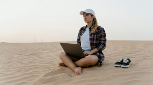 How to Keep Your Business Running While You Travel - Woman on Laptop on a Beach 4 Easy Beach Frizz Solutions for Humid Beach Days