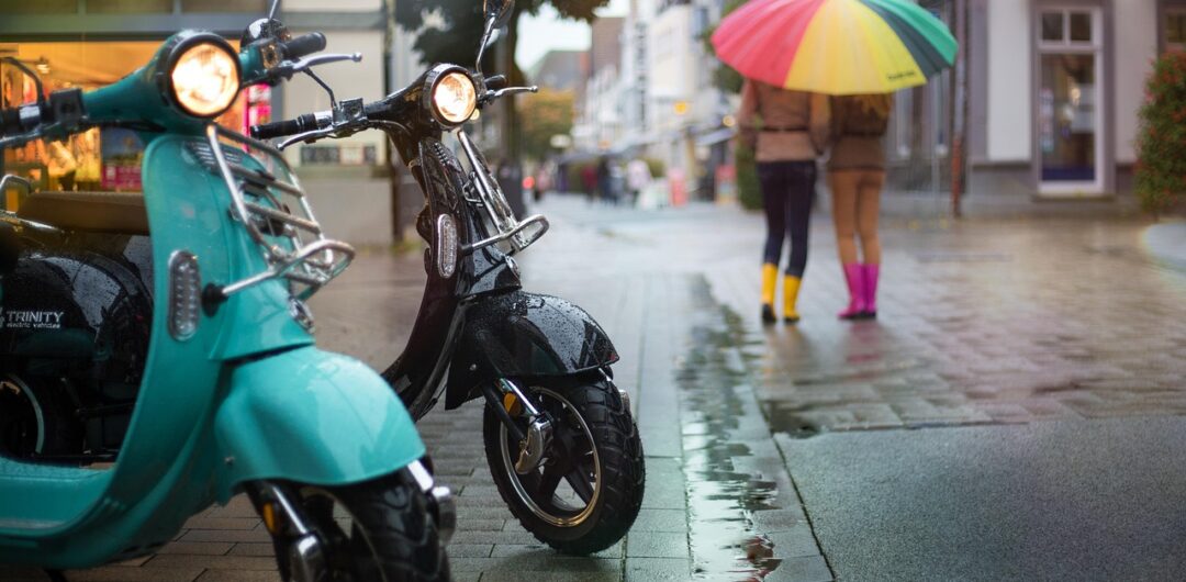 4 Reasons a Scooter Is Perfect for Short Trips - Two Scooters in the Rain with Two Women in the Background